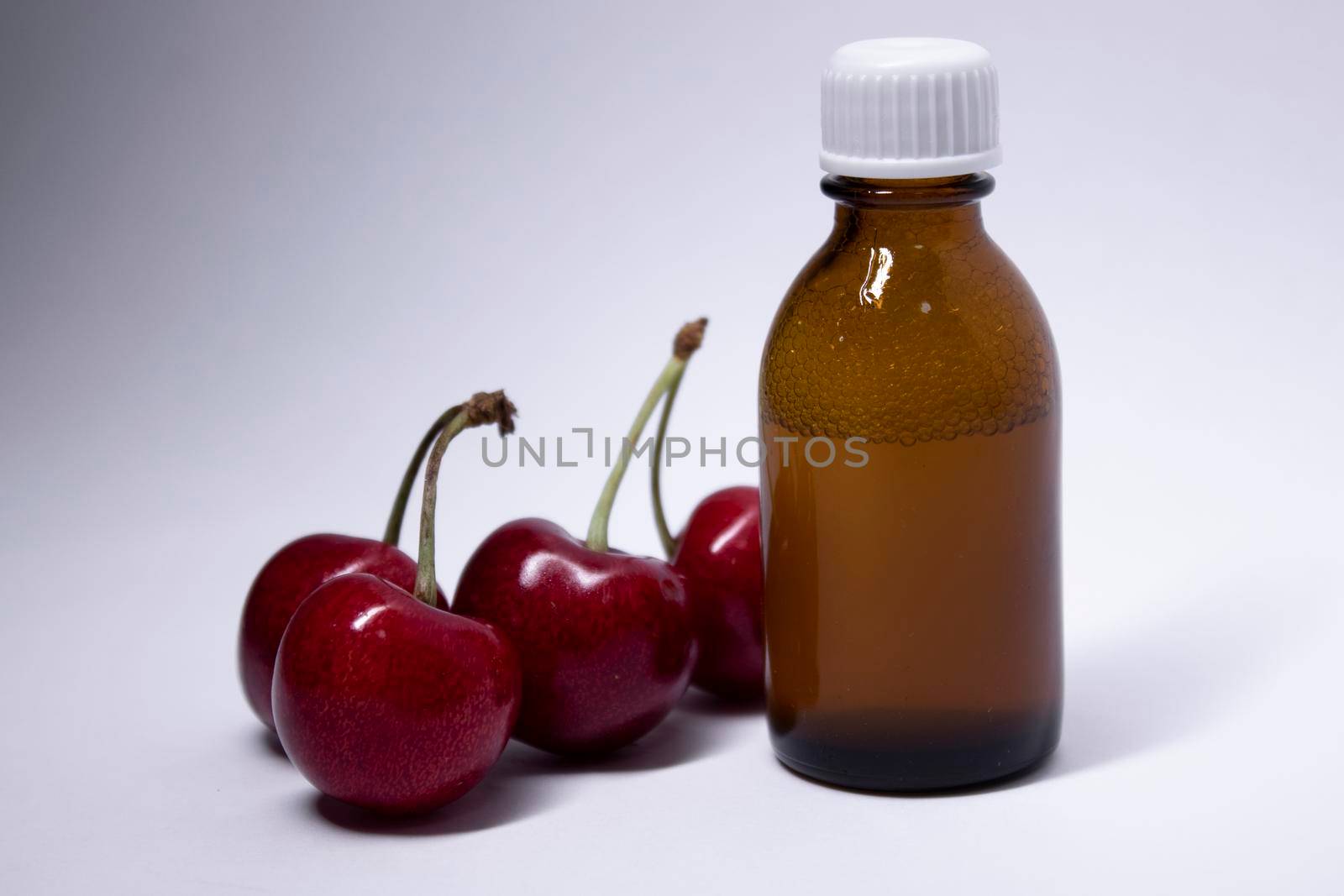 little liquid bottle with no label near cherry. body care and beauty concept. Copy space. High quality photo