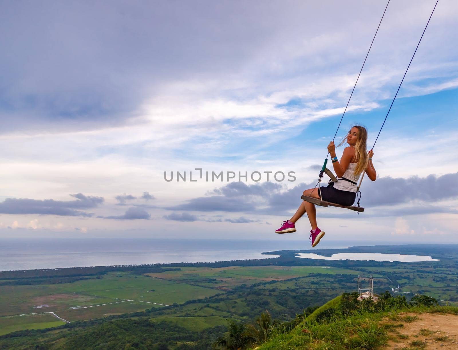 A young girl, blonde, swinging on a swing on a mountain slope in summer. by Yurich32