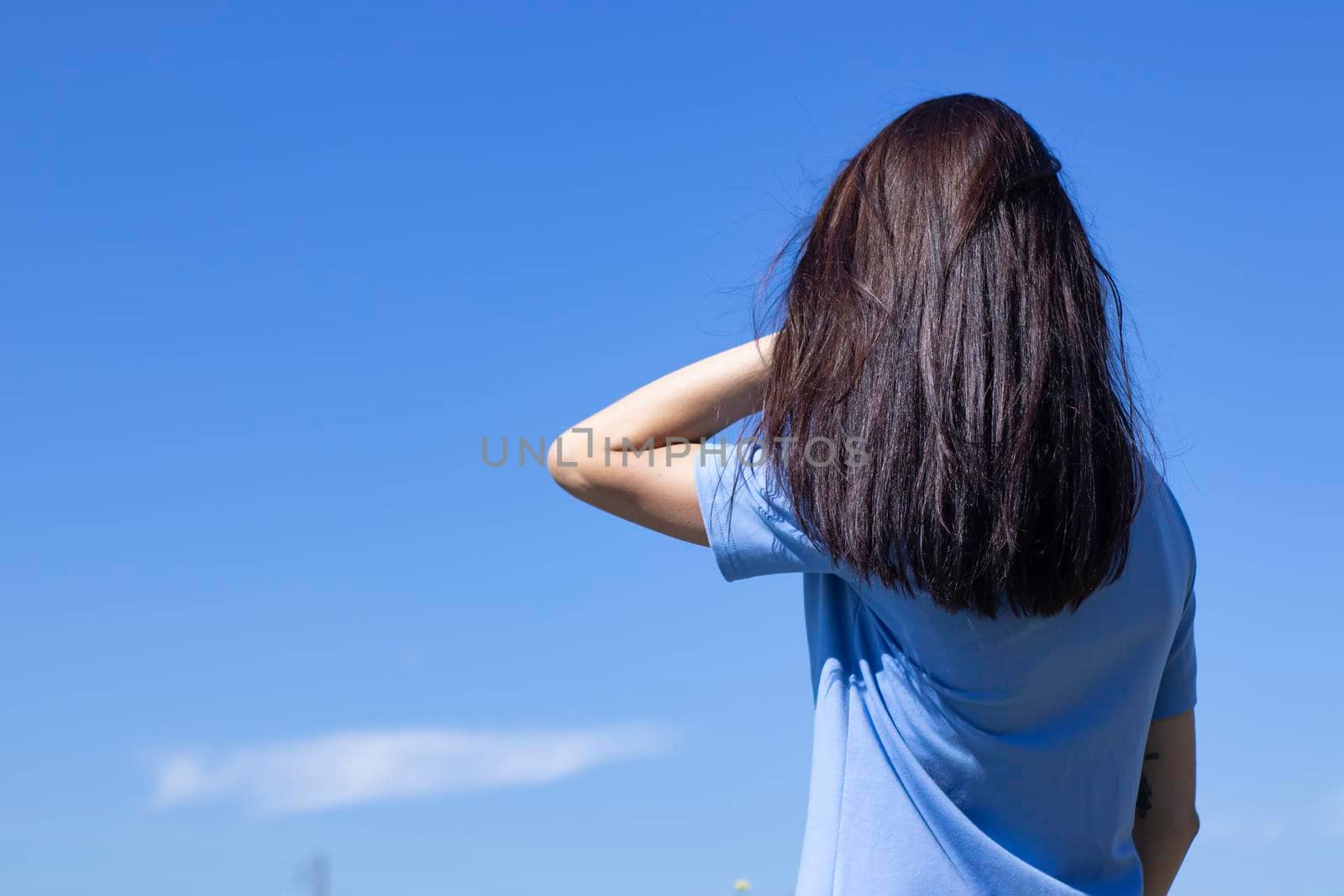 slim brunette girl in a blue dress standing with her back to us in front of a beautiful blue sky. High quality photo