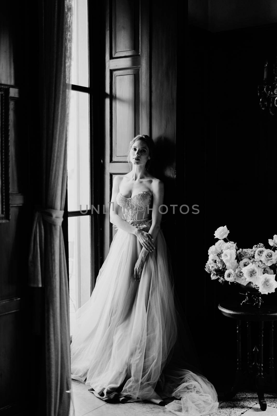 Bride is leaning against the frame of the large window of an old villa. Lake Como. Black and white photo. High quality photo