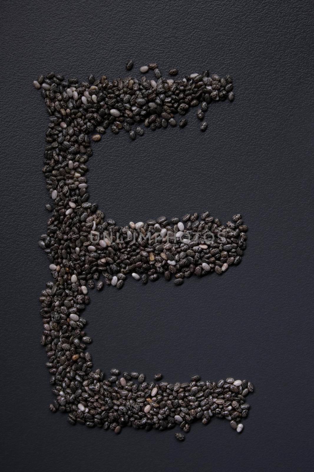 Letter 'E' written with chia seeds on gray background, top view, copy space.