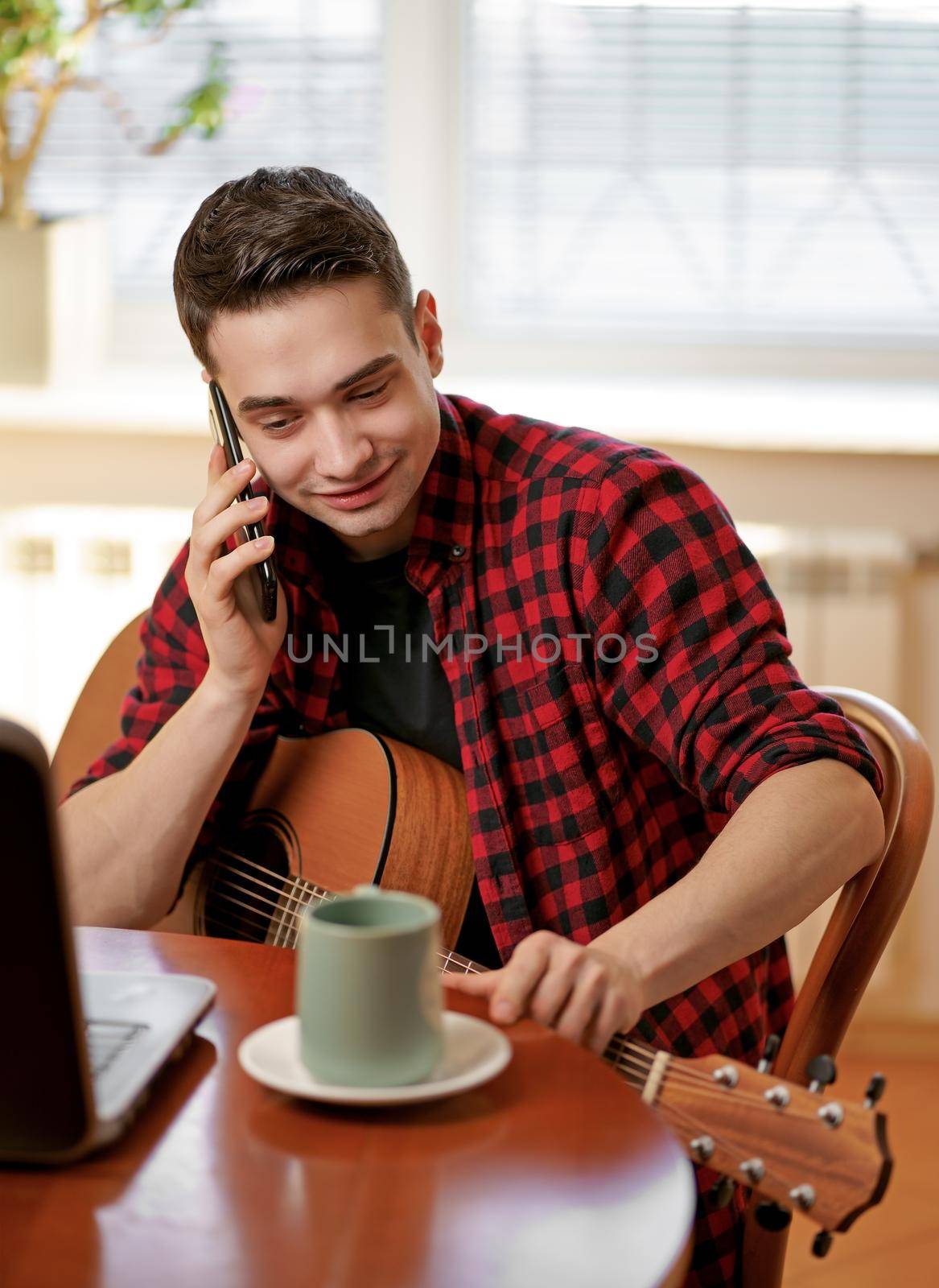 A young man learns to play the guitar using the Internet, laptop, online lesson. Hobby and leisure concept by aprilphoto