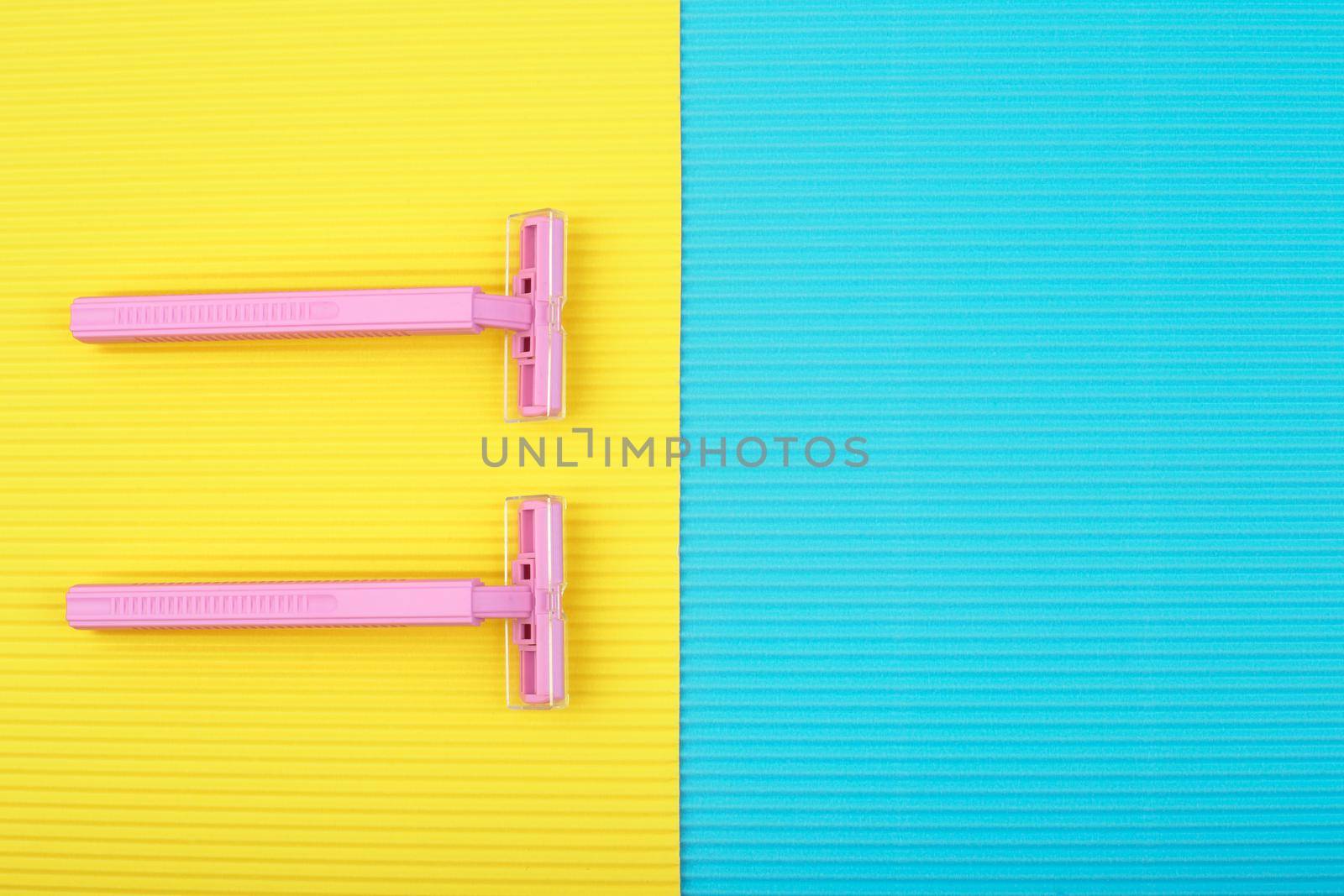 Top view of pink razors against yellow and blue background with space for text. Concept of smooth skin, shaving and depilation