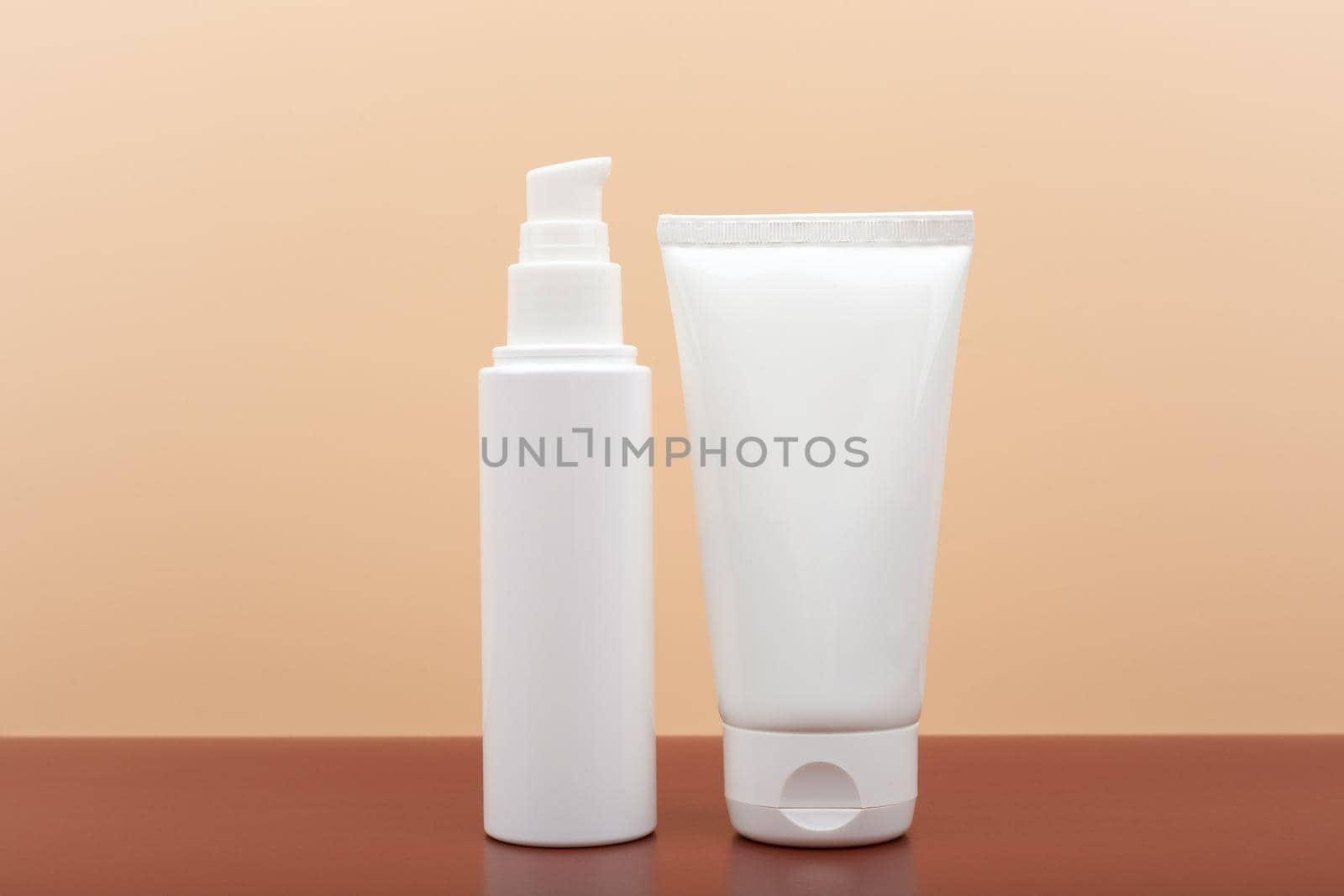 Two white cream tubes on brown table against beige background. Concept of skin care and beauty