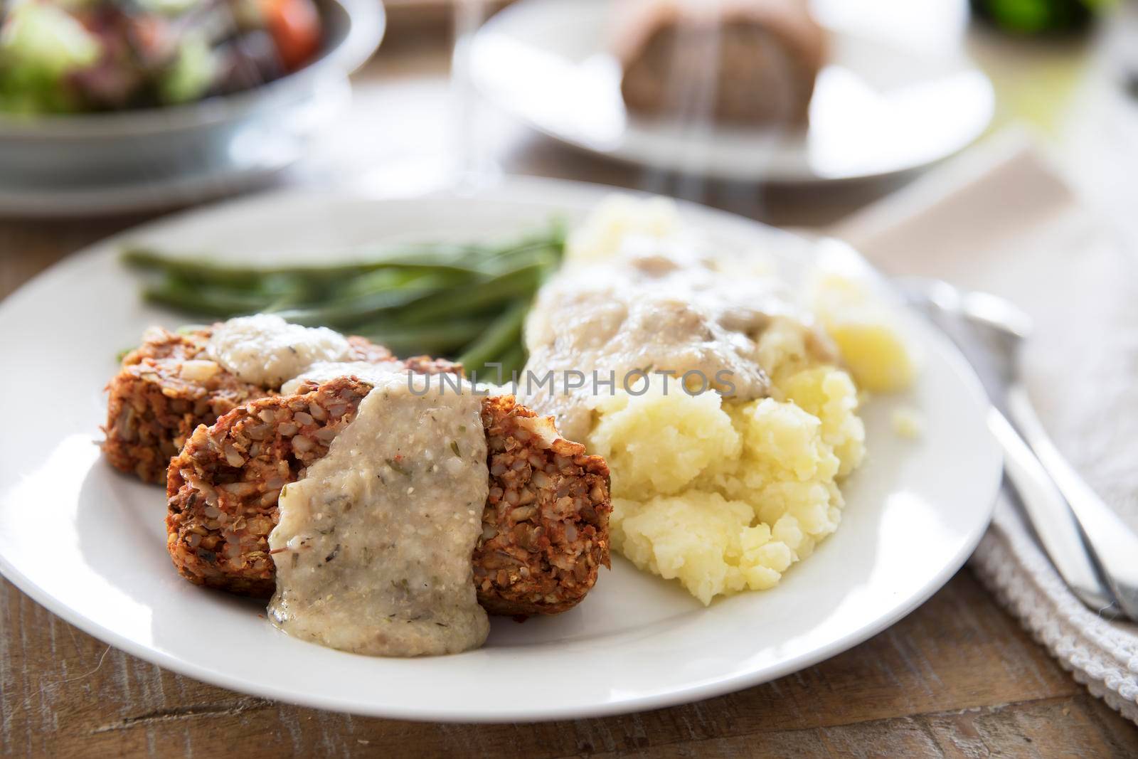 Slices of vegan lentil loaf covered in gravy with mashed potatoes and green beans.
