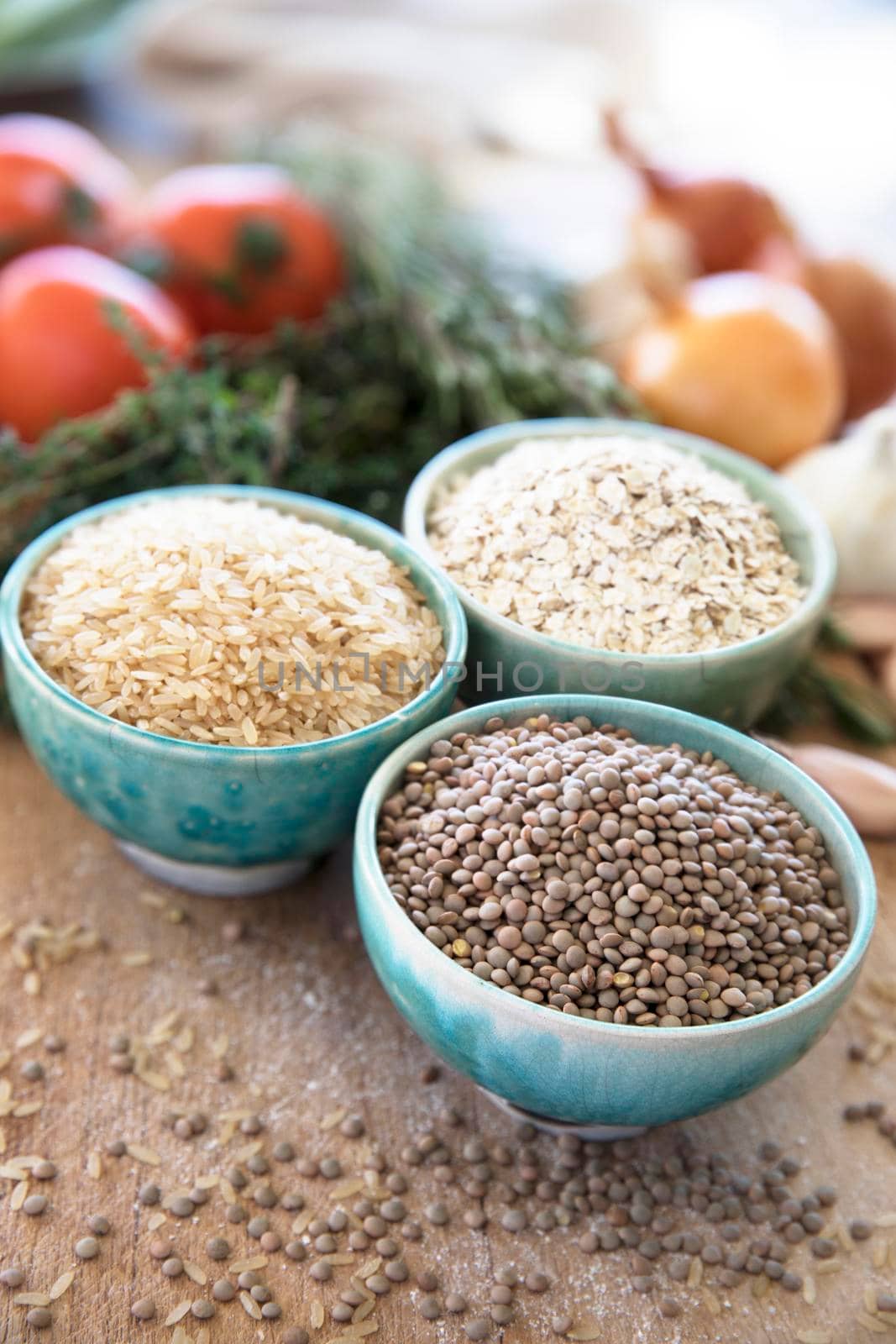Healthy grains:  lentils, brown rice, and oats in bowls with veggies in the background.