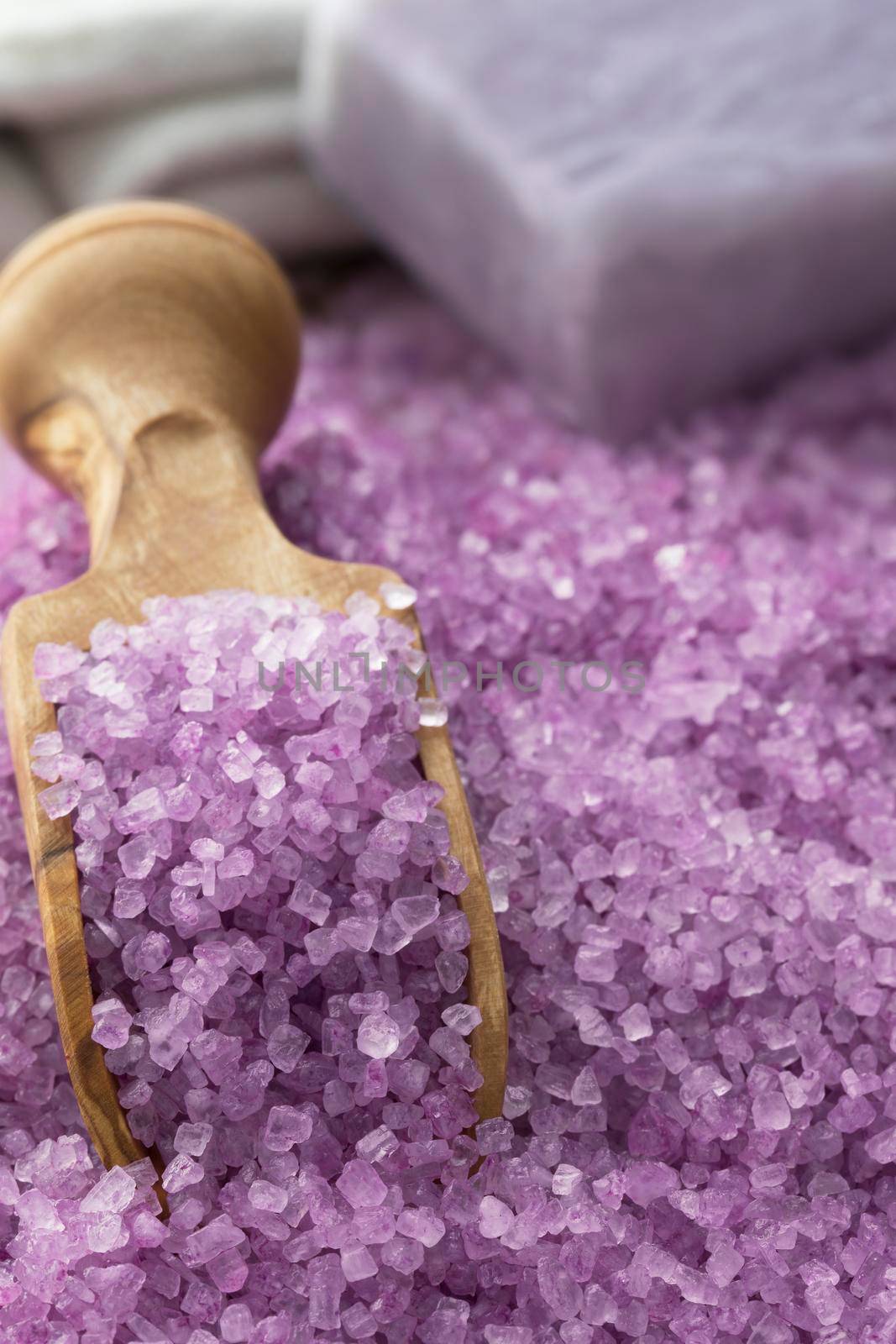 Purple bath salts with wooden scoop and soap in background