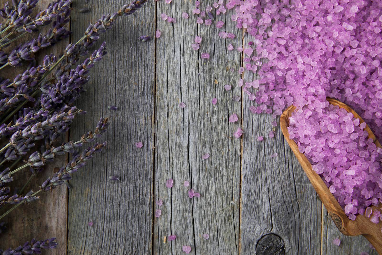 Purple bath salts with wooden scoop on wooden surface with copy space