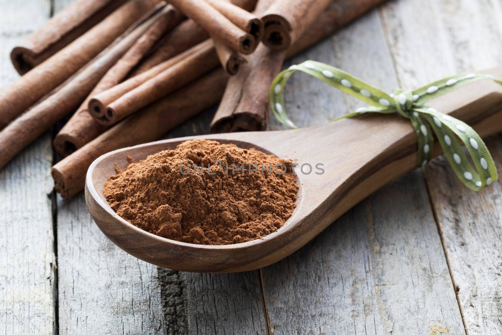 Close up of wooden spoon filled with ground cinnamon in front of  cinnamon sticks.