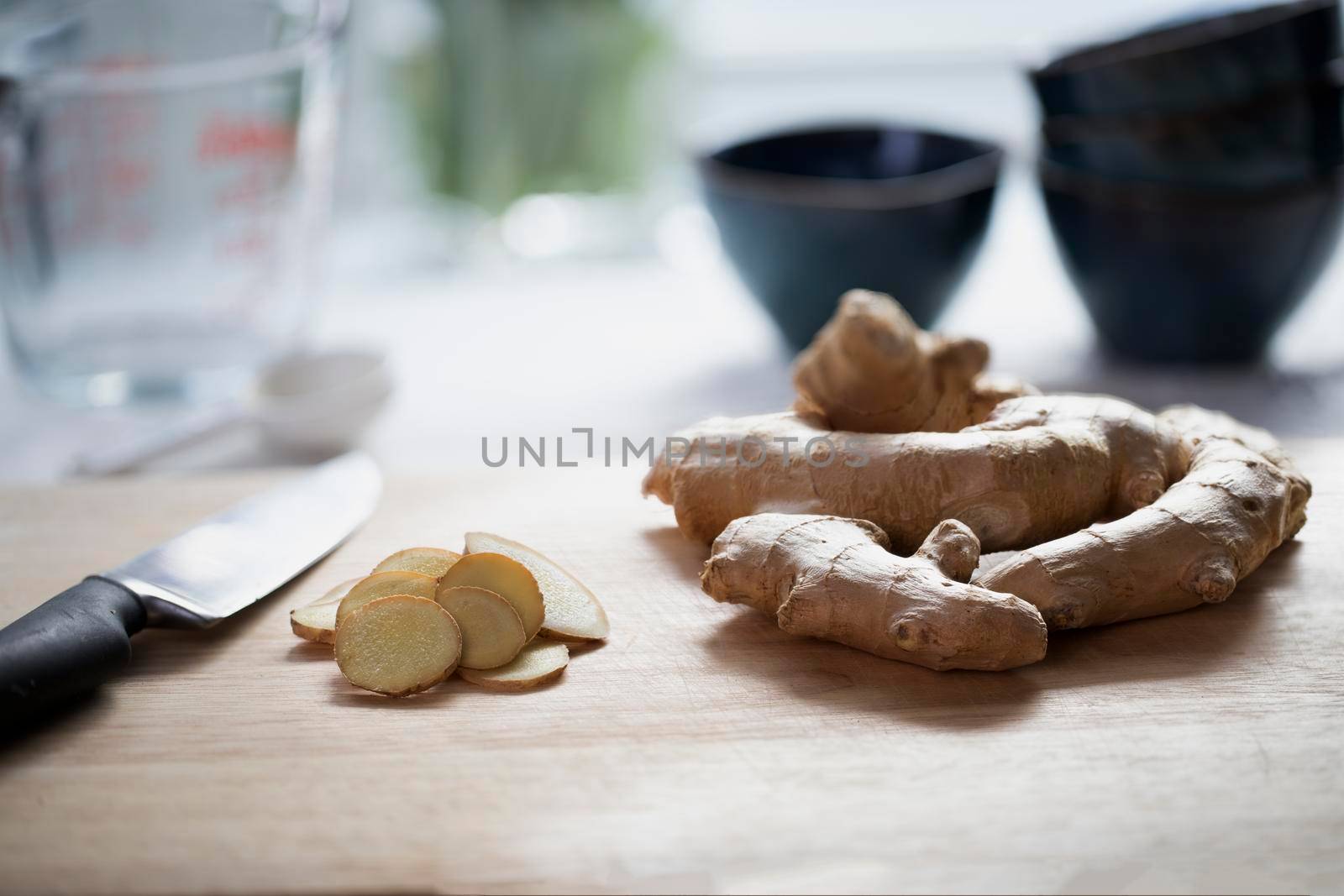 Ginger root and ginger slices with knife on cutting board.