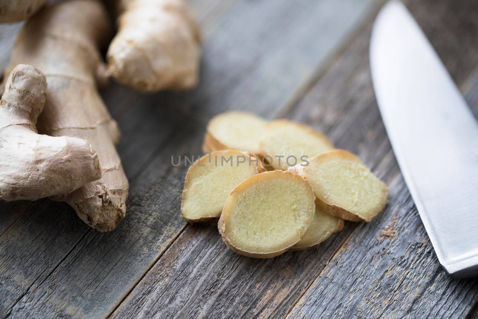 Ginger root and ginger slices with knife on cutting board.