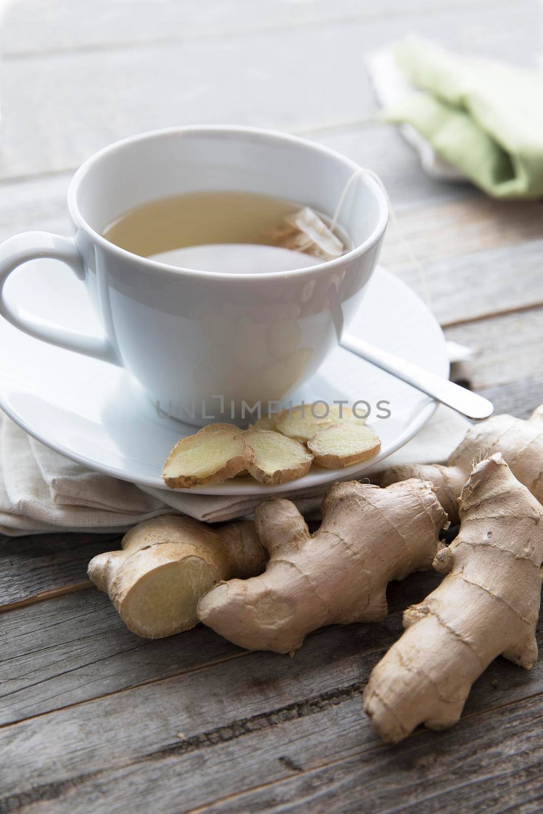 Cup of hot ginger tea with ginger slices and ginger root, vertical orientation.