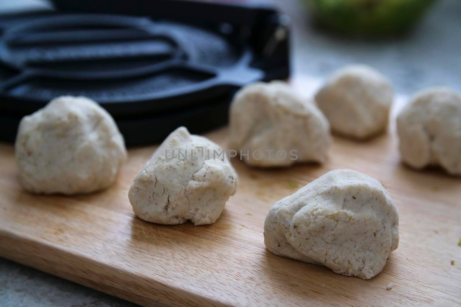 Masa Harina tortilla dough on cutting board with tortilla press in background.