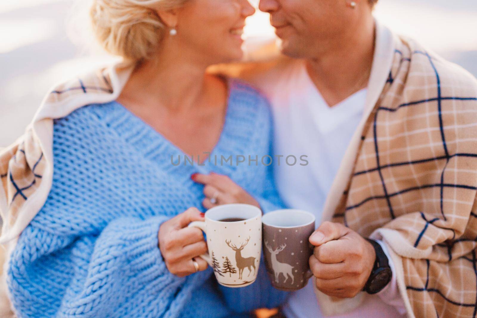 Smiling couple wrapped in a plaid and holding cups in their hands on a background of mountains. High quality photo