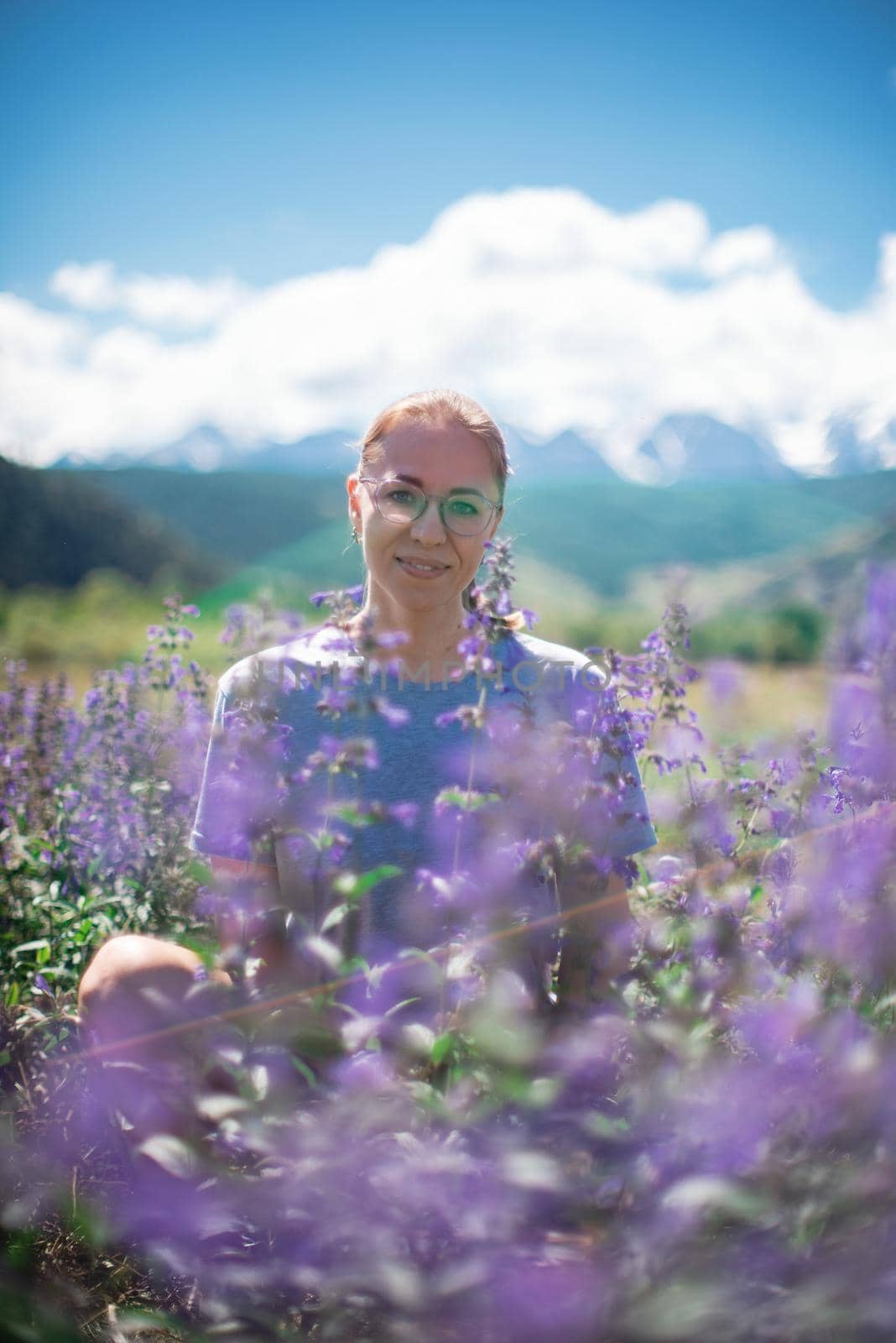 Happy young woman in beautiful wild pink and purple flowers field in summer Altai mountains