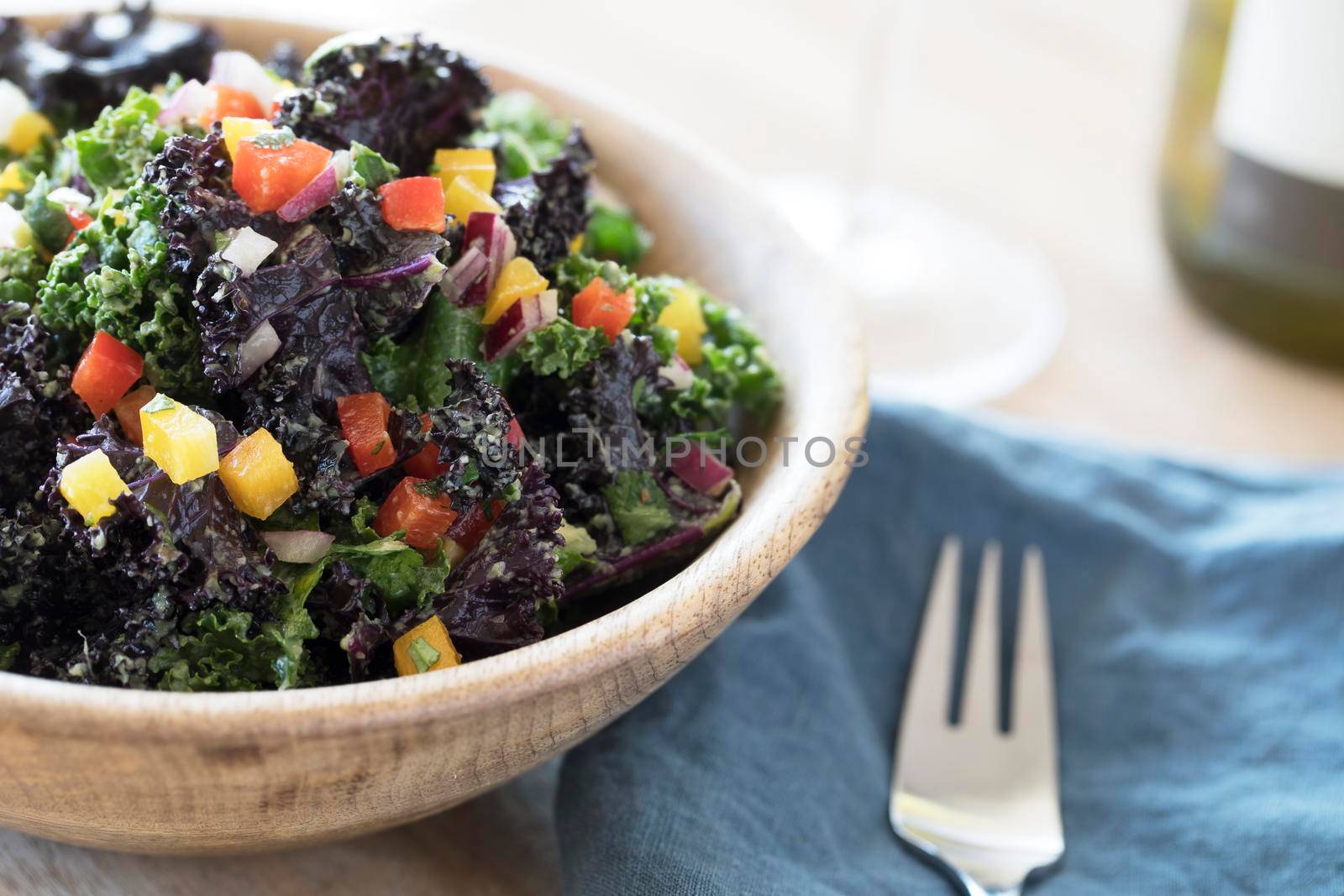 Healthy kale salad with fresh bell peppers and red onions in a wooden bowl.