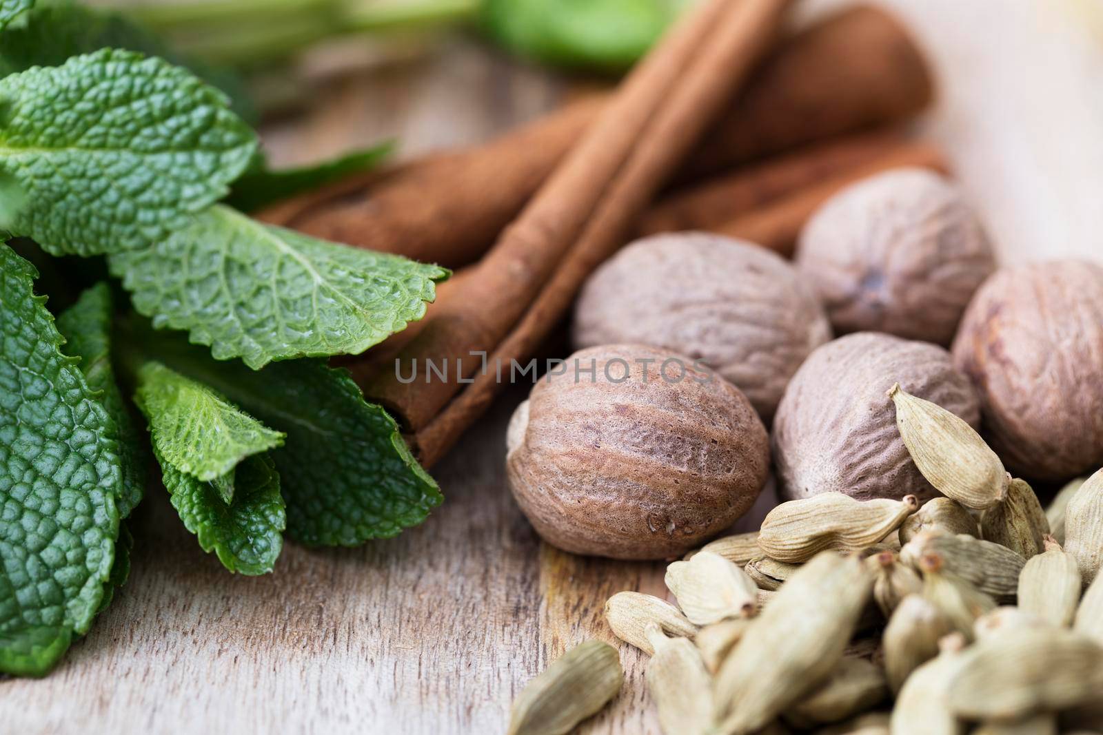 Cardamon, nutmeg, mint leaves and cinnamon sticks close-up on rustic wooden surface