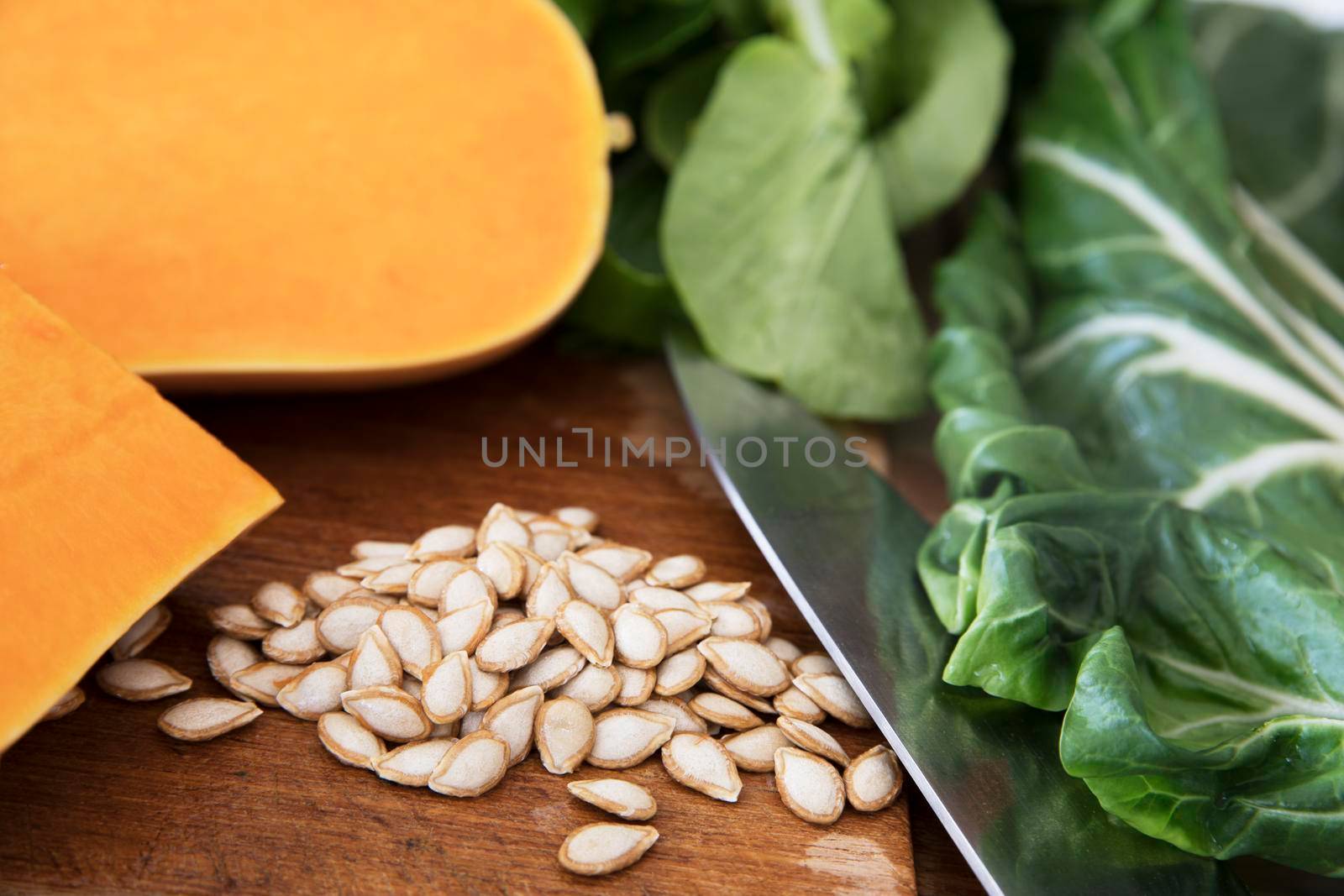 Butternut squash seeds on a cutting board with a knife, pieces of butternut squash and chard.