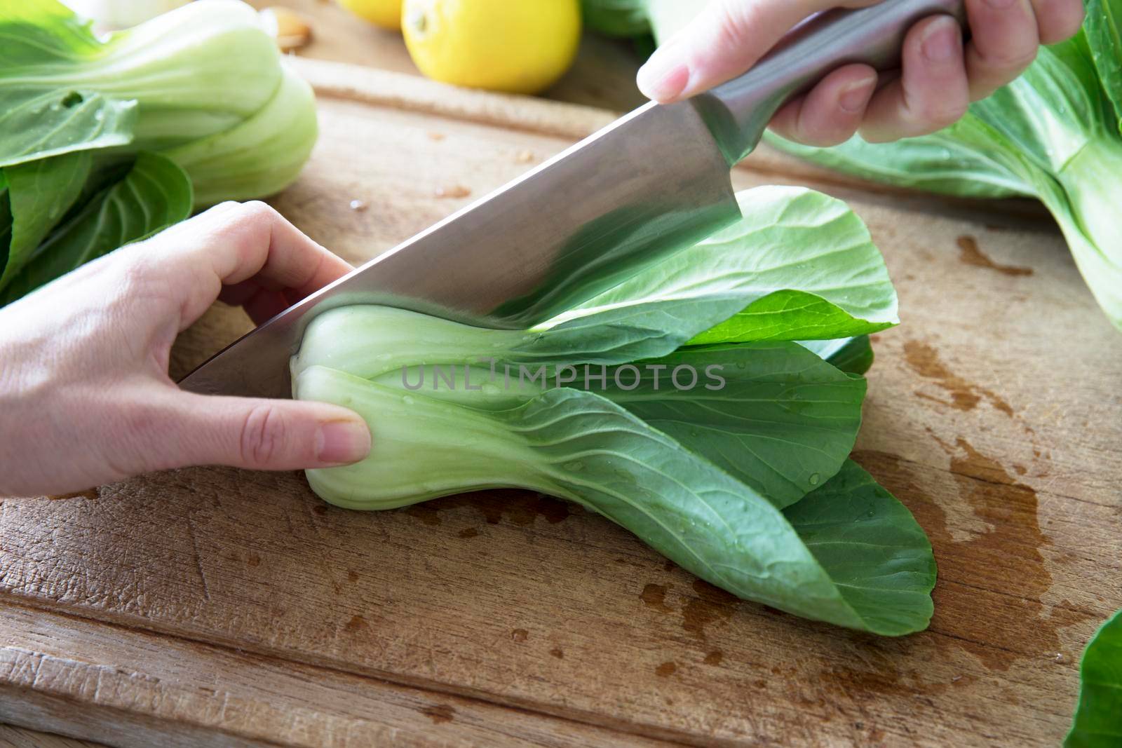 Slicing boy choi in half  with chef's knife on cutting board.