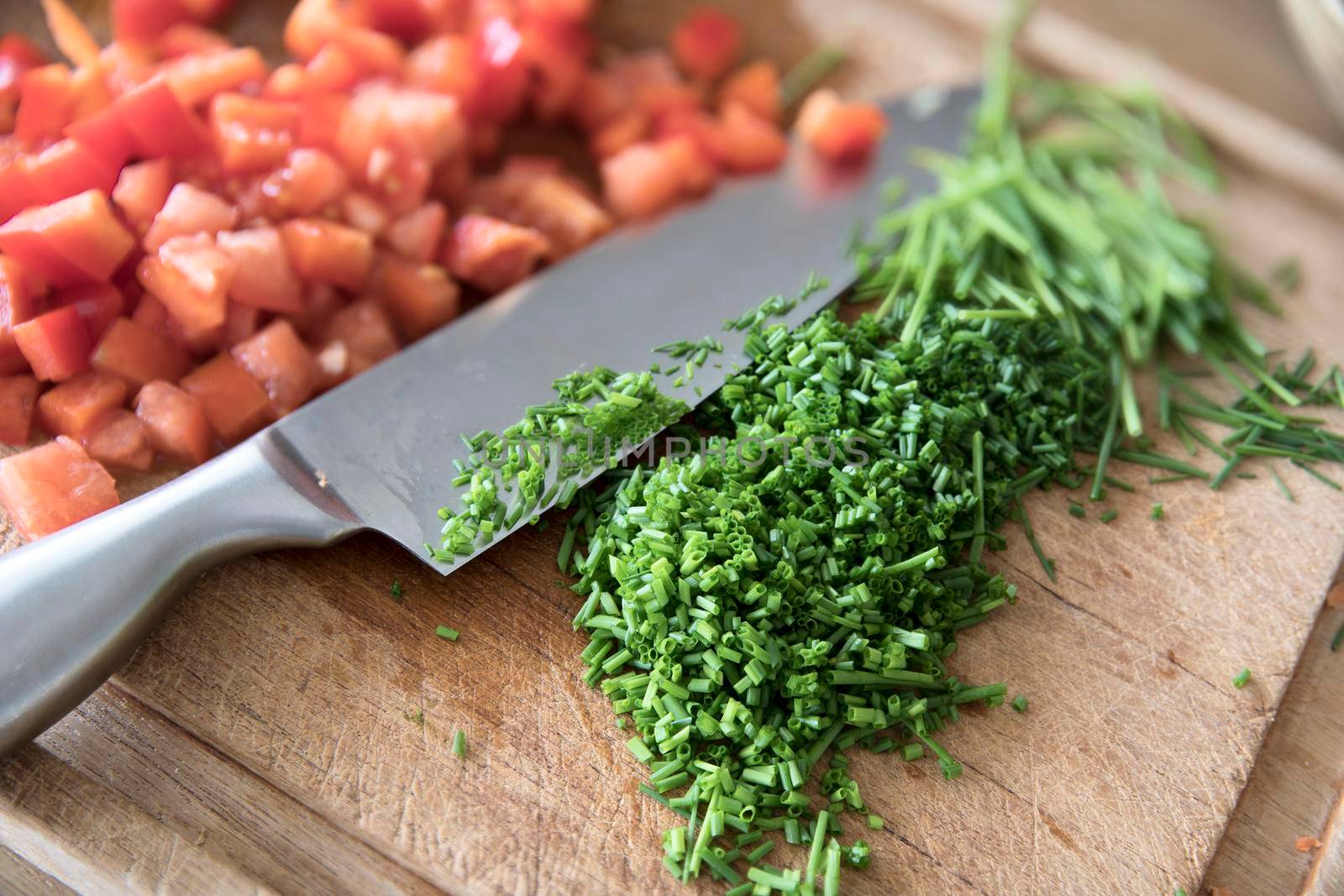 Chopped chives on cutting board with chef's knife and chopped tomatoes