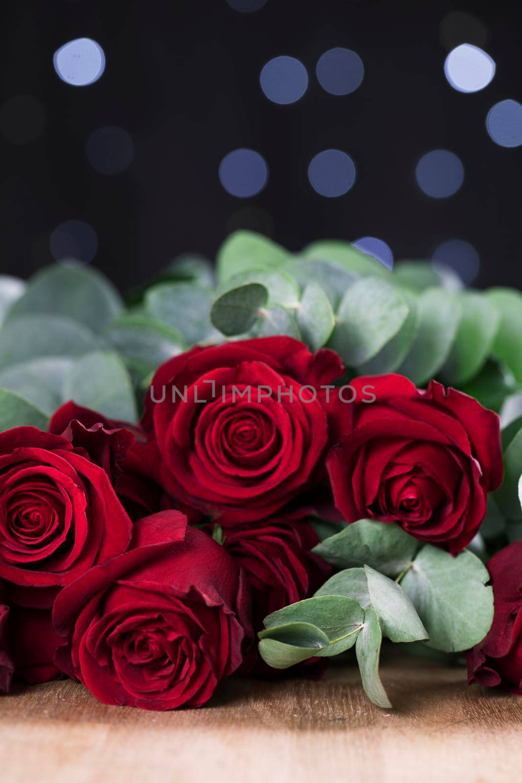 Vibrant red roses with lights in the background, vertical orientation.