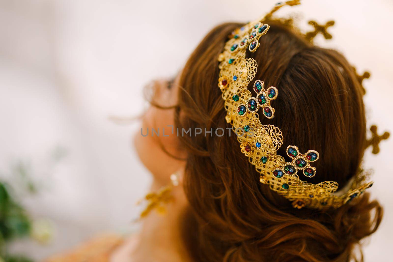 A woman with a beautiful hairstyle in a gold crown with stones, close-up. Bride wearing a crown on an orthodox wedding . High quality photo
