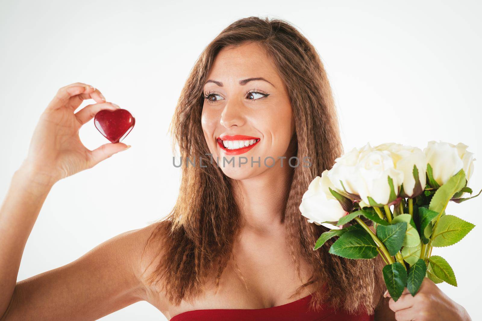 Portrait of a beautiful smiling girl holding a red heart and bouquet of white roses.
