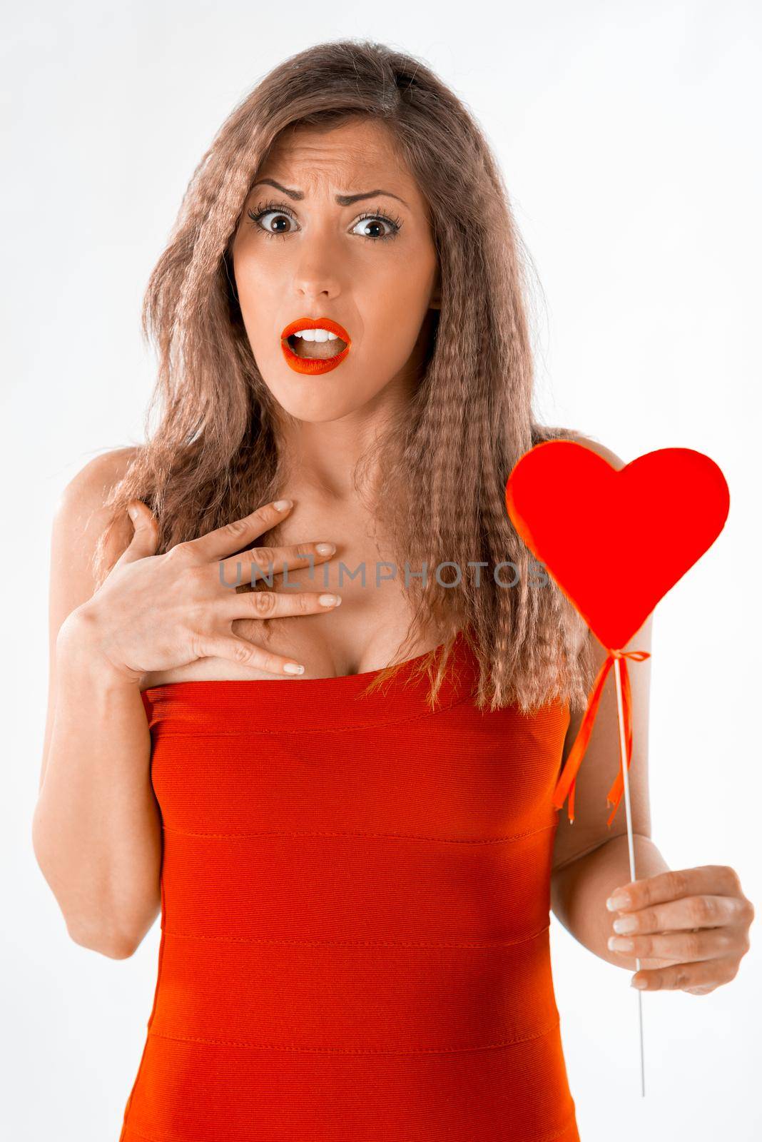Beautiful surprised girl holding a red heart. Looking at camera.