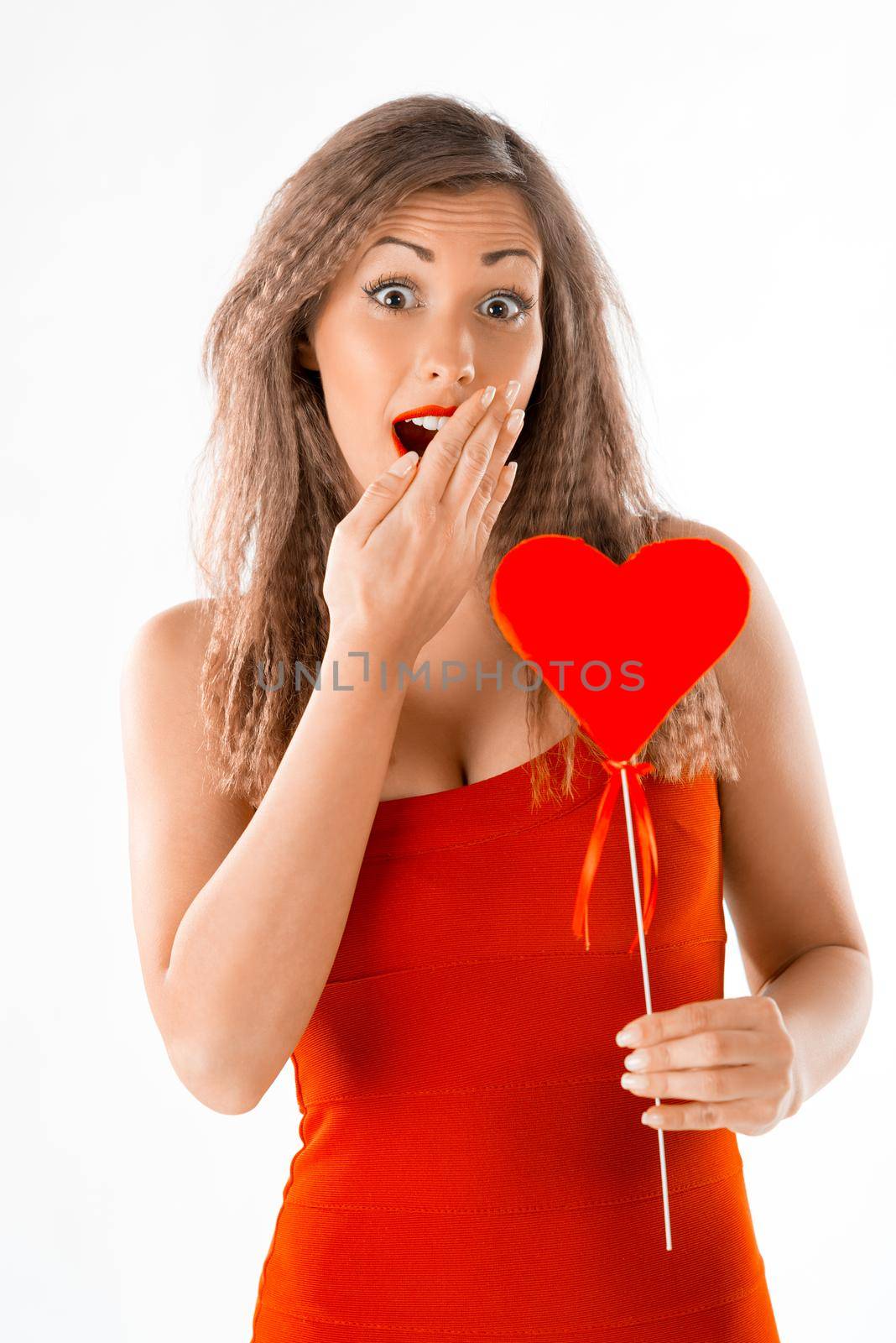Beautiful surprised girl holding a red heart. Looking at camera.