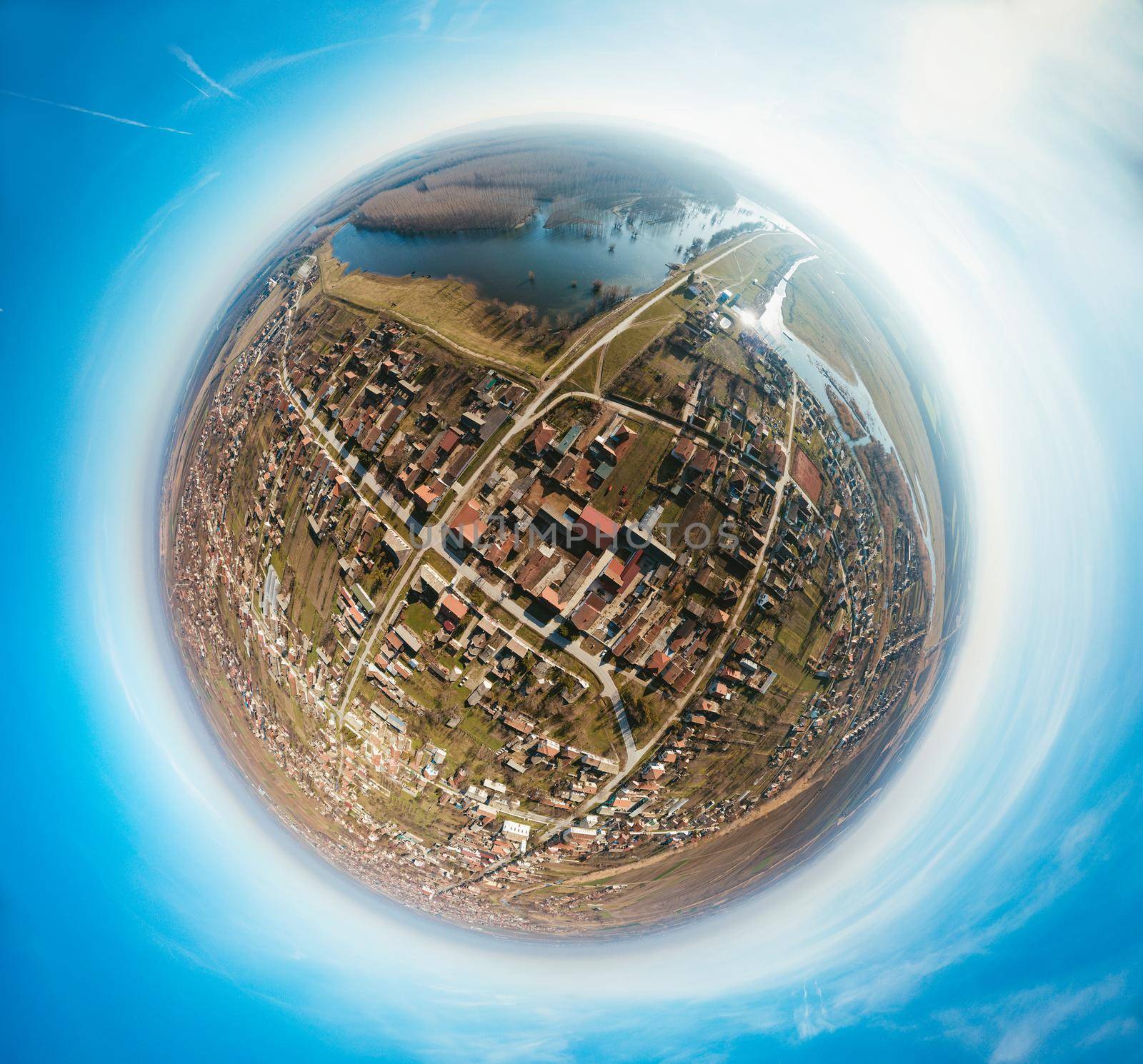 Panorama of the village in the river's valley in a form of a little planet on a blue sky background.