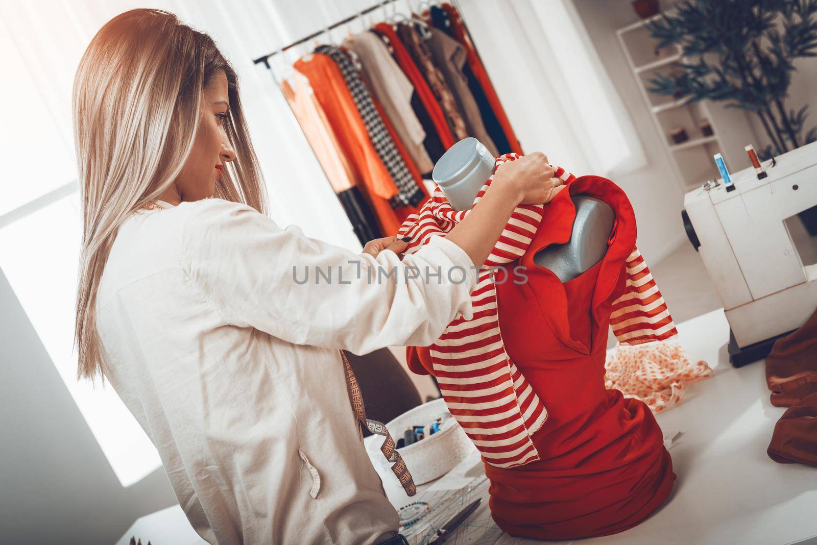 Young female fashion designer creates a dress on mannequin. 