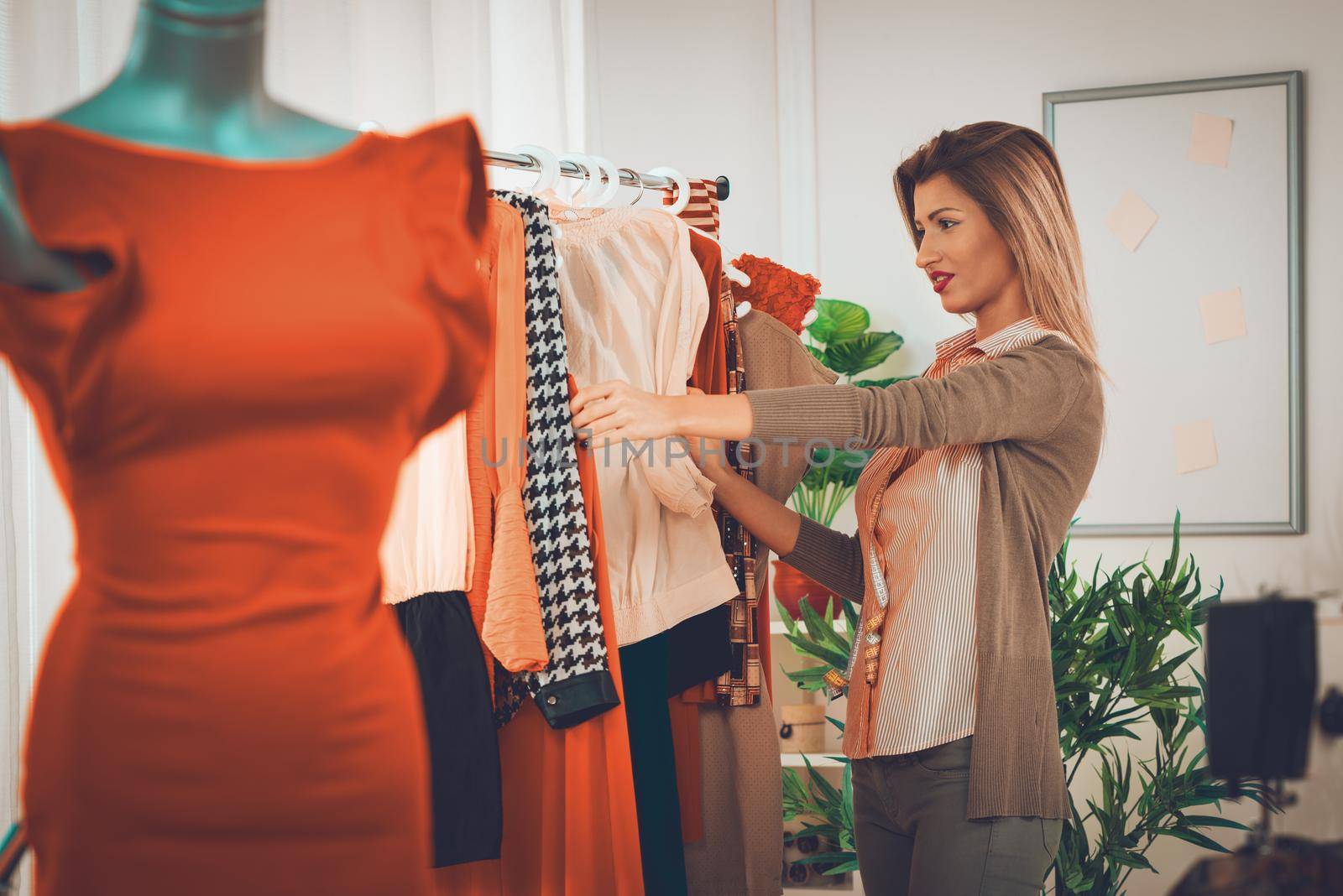 Beautiful young woman choosing clothing at the fashion designer office. In the foreground you can see a dress on mannequin. Selective focus. Focus on background.