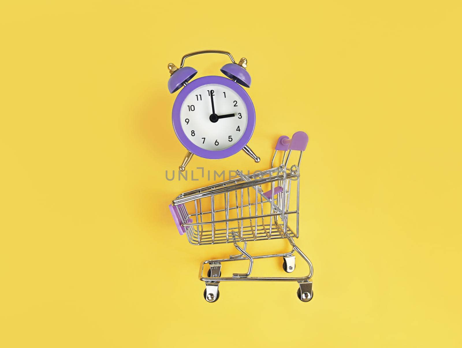 Supermarket trolley and violet alarm clock on a yellow background. Buy time, busy concept.