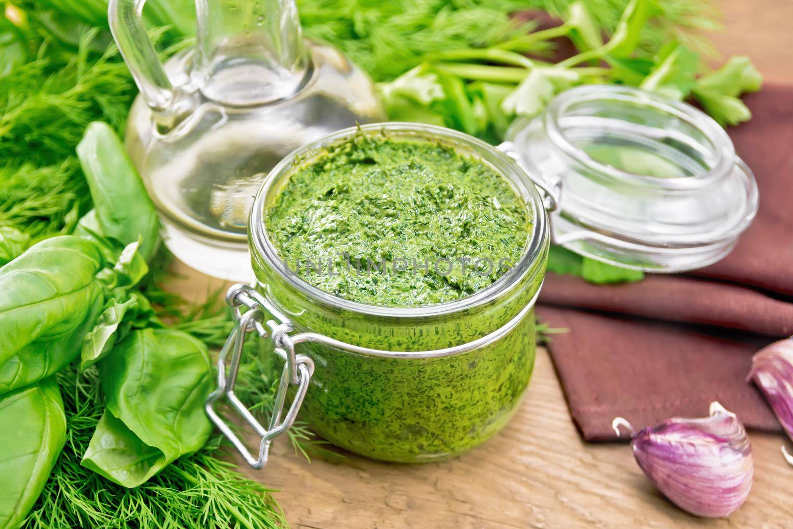 Sauce of dill, parsley, basil, cilantro, other spicy herbs, garlic and vegetable oil in a glass jar, a towel on wooden board background