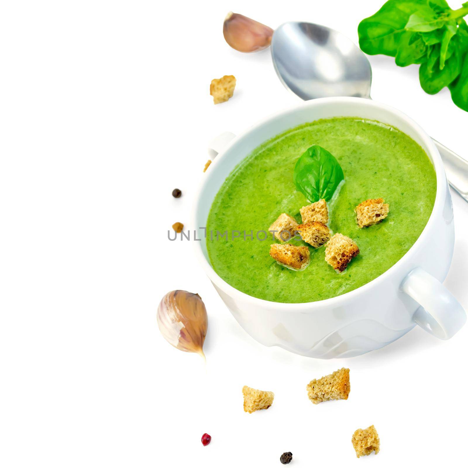 Green soup puree in a white bowl with crackers, spinach, spoon, garlic, pepper isolated on white background