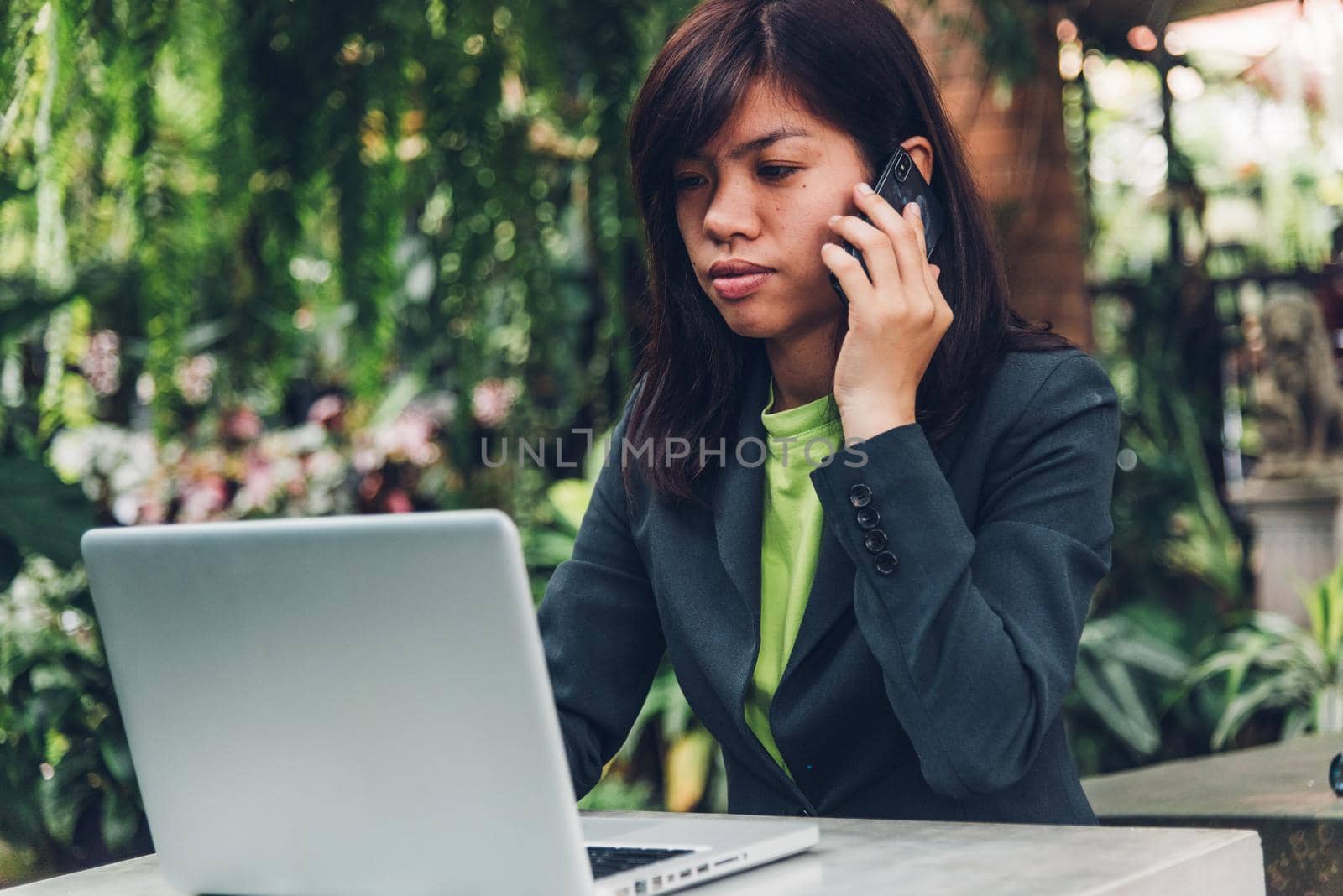 Young businesswoman talking on mobile smart phone with his client. He works on a laptop computer on the desk