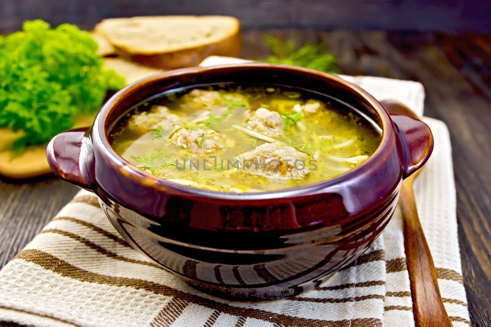 Soup with meatballs and noodles in pottery on board by rezkrr