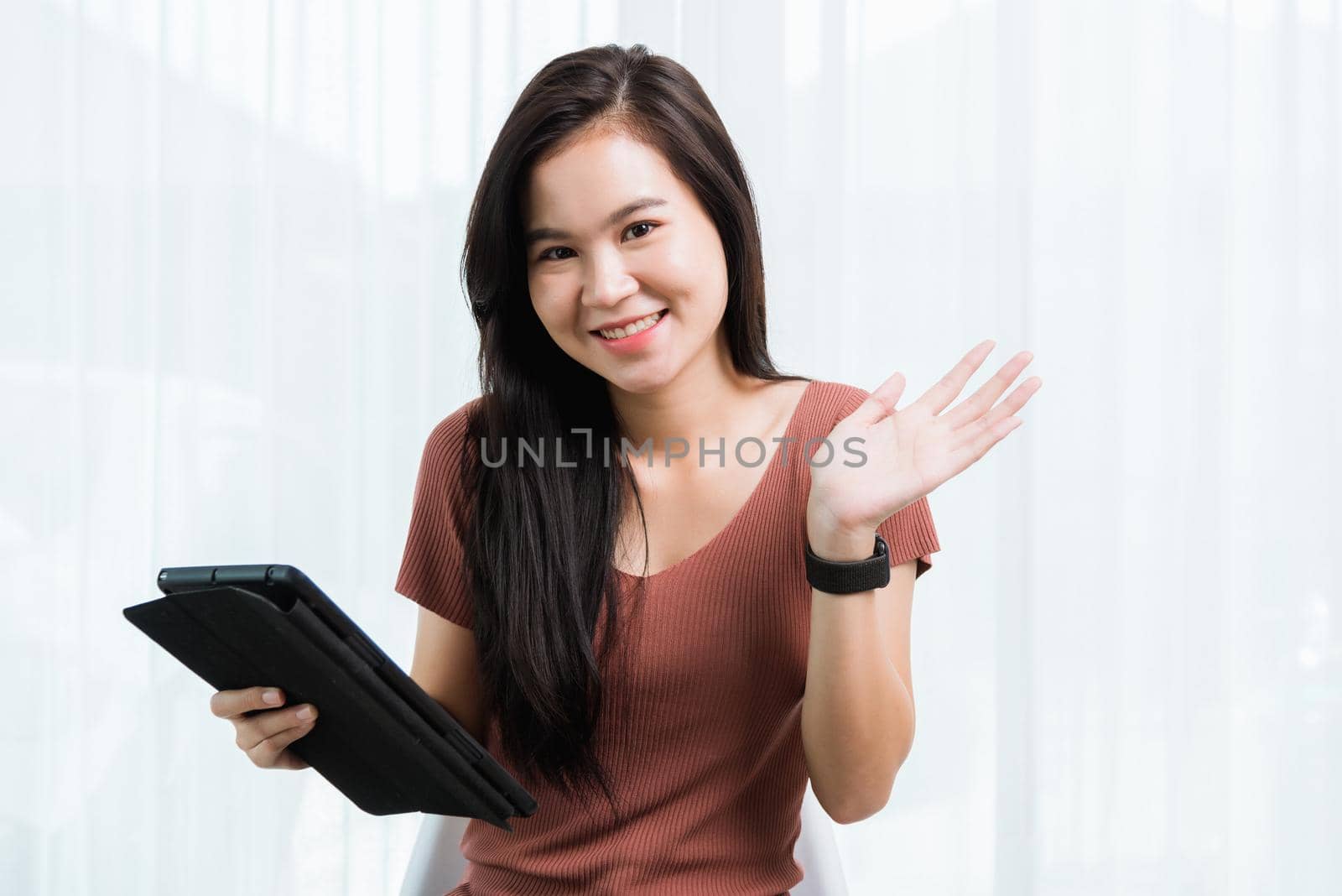 Work from home, Happy Asian young businesswoman smile video conference call or facetime by modern digital smart tablet computer she raises a hand and says hello on screen at the home office