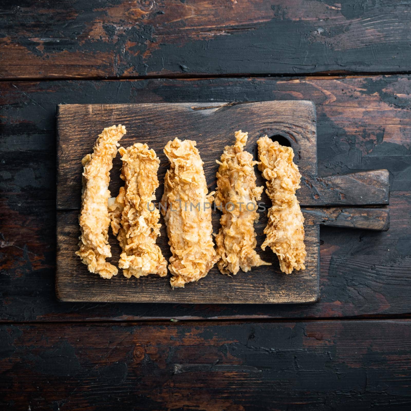 Crispy chicken sticks meat on dark wooden background, top view.