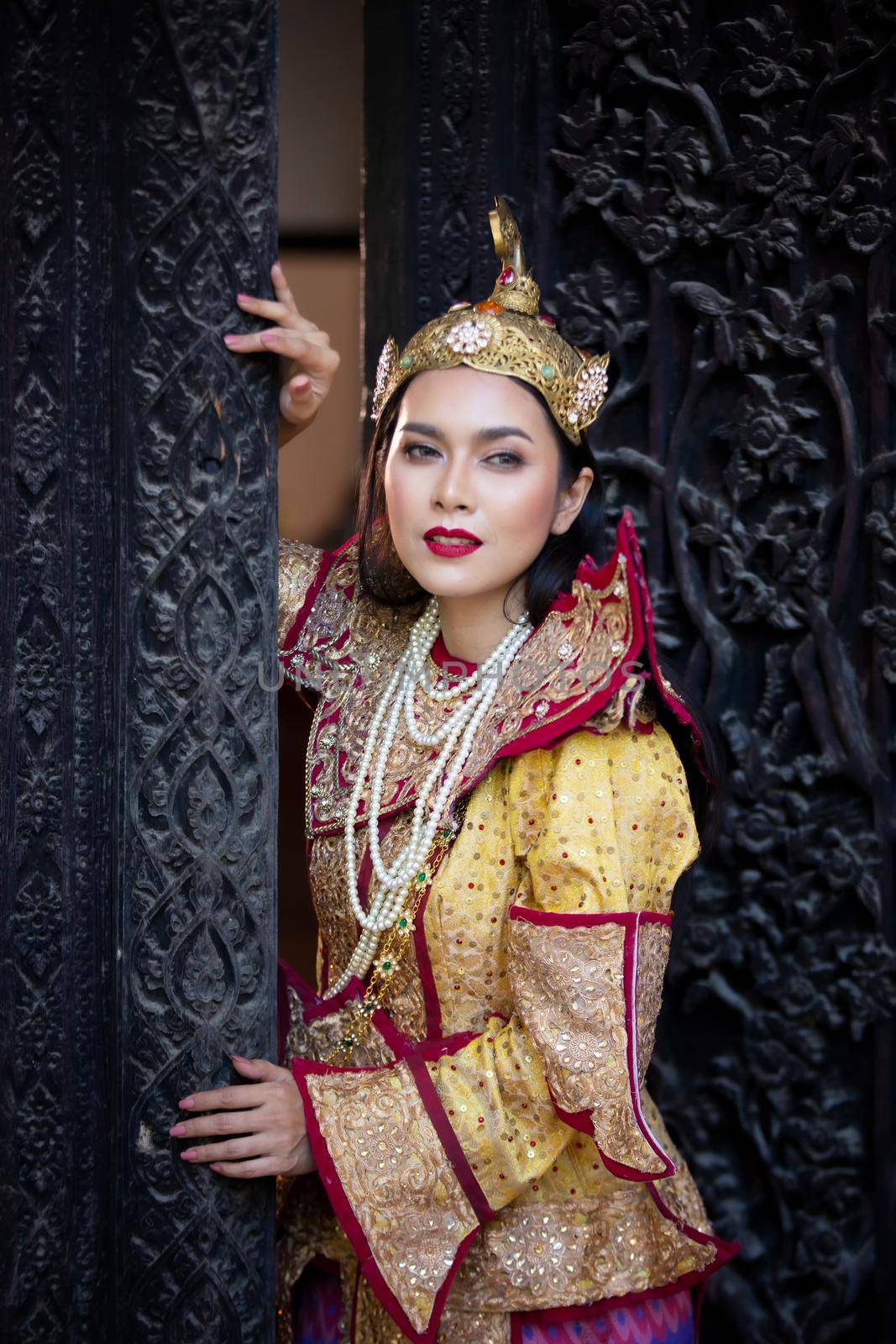 Portrait of an Asian Women in Mandalay, Myanmar Woman with golden Traditional Clothes are Standing Against Art Carving Wooden Door. by chuanchai