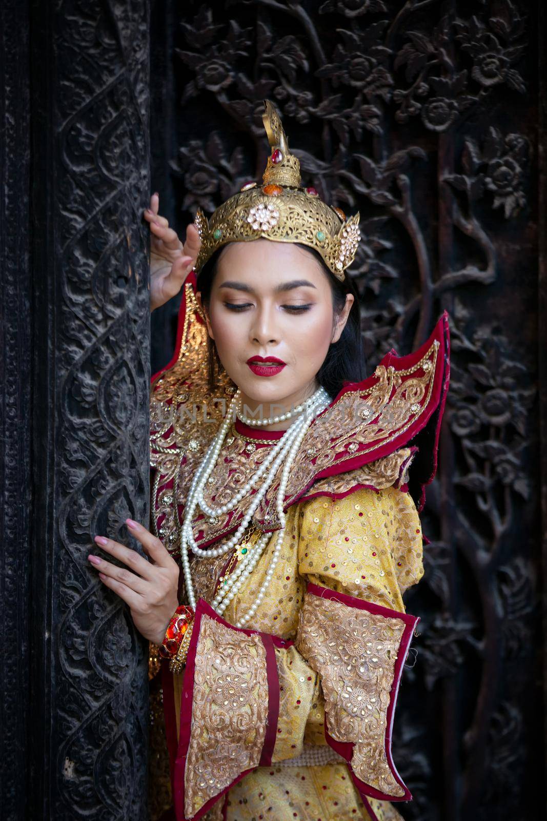 Portrait of an Asian Women in Mandalay, Myanmar Woman with golden Traditional Clothes are Standing Against Art Carving Wooden Door. by chuanchai