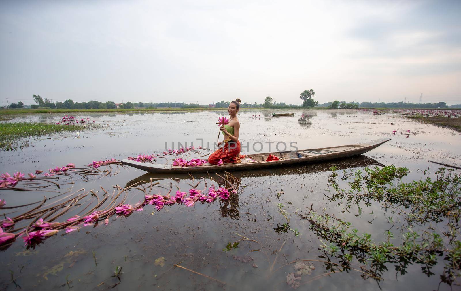 Young Asian women in Traditional dress in the boat and pink lotus flowers in the pond.Beautiful girls in traditional costume.Thai. Ayutthaya, elegance.