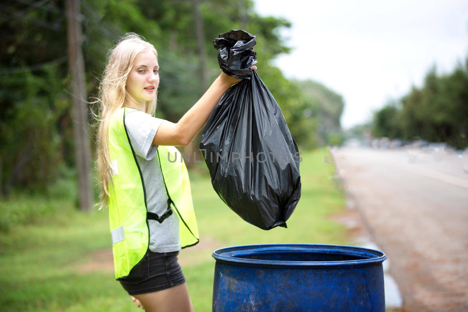 Green volunteering. Optimistic two volunteers holding garbage bag and help picking up trash at park, they're picking up the garbage and putting it in a black garbage bag. ecology protection concept.