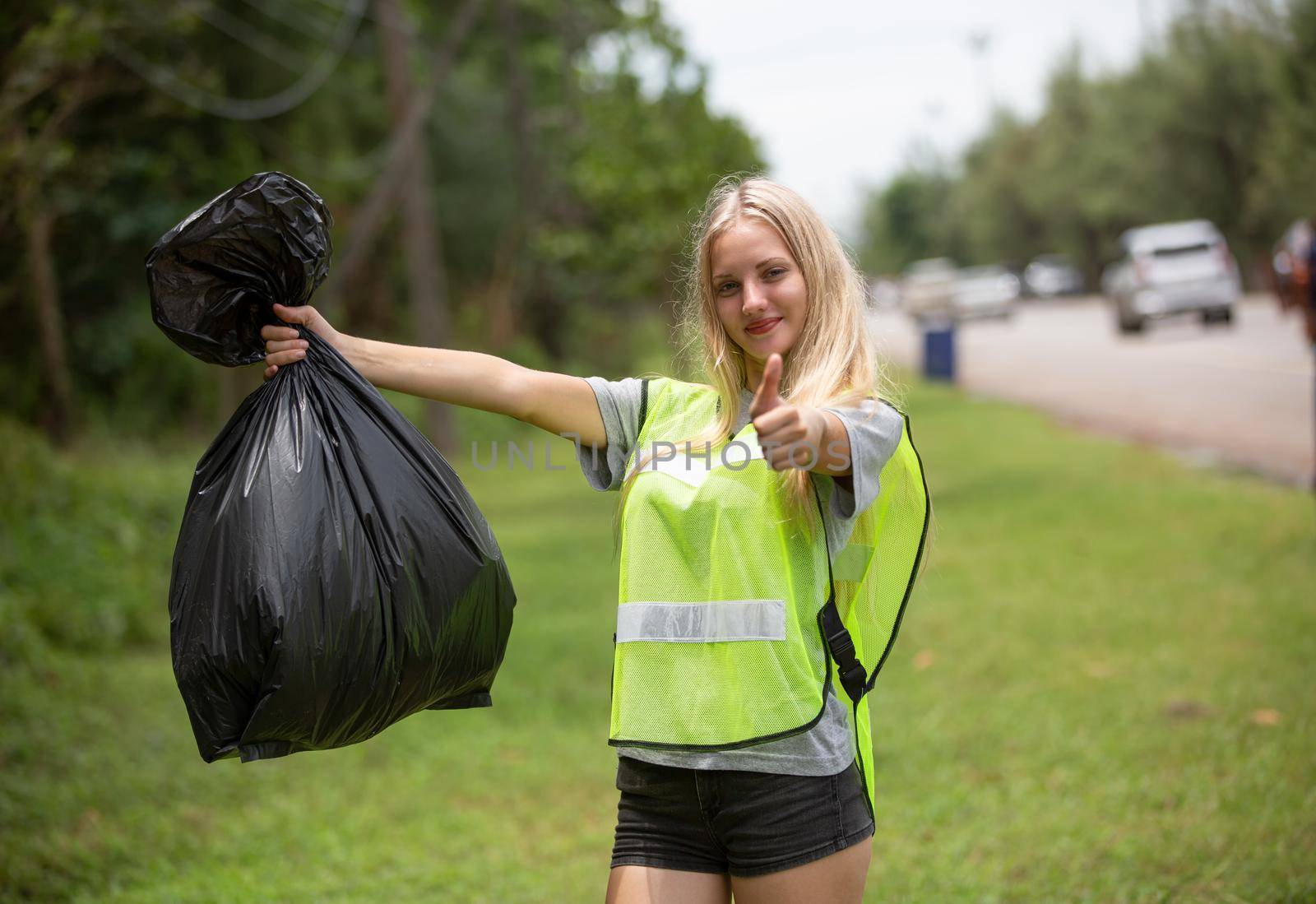 Green volunteering. Optimistic two volunteers holding garbage bag and help picking up trash at park, they're picking up the garbage and putting it in a black garbage bag. ecology protection concept. by chuanchai