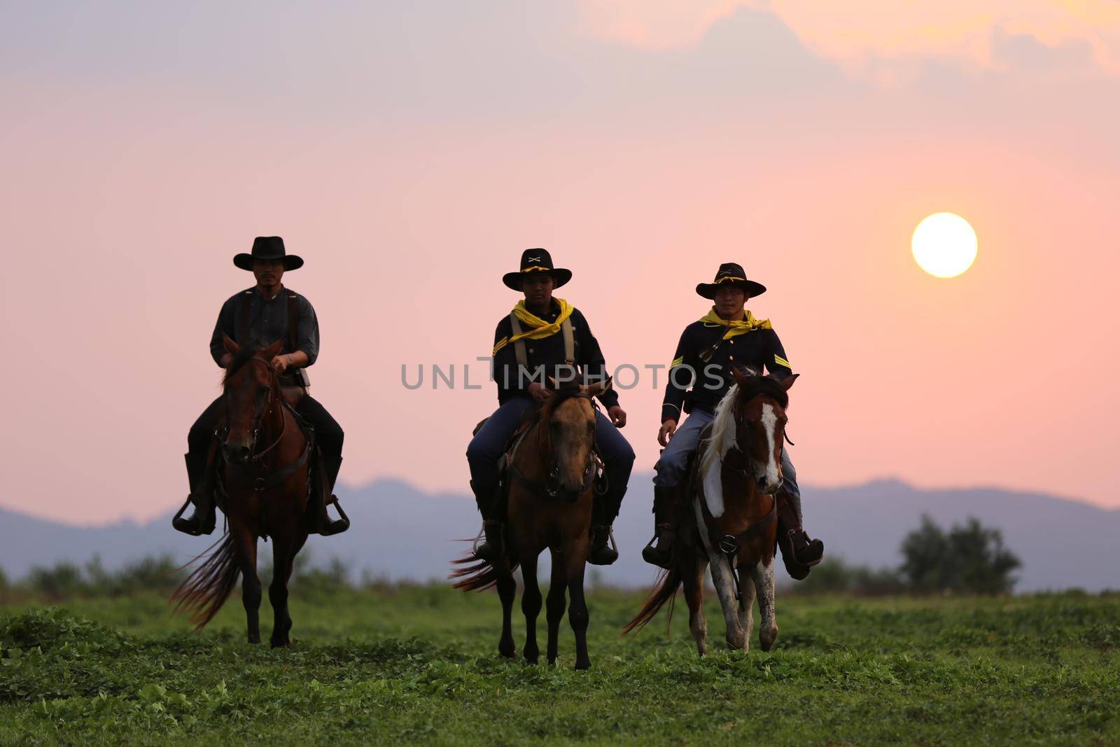 The silhouette of rider as cowboy outfit costume with a horses and a gun held in the hand against smoke and sunset background