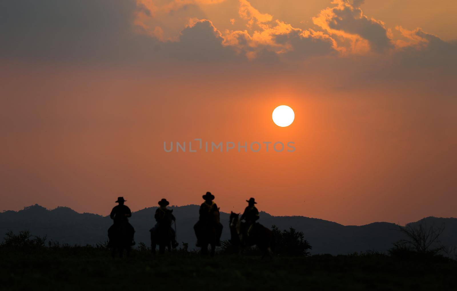 The silhouette of rider as cowboy outfit costume with a horses and a gun held in the hand against smoke and sunset background