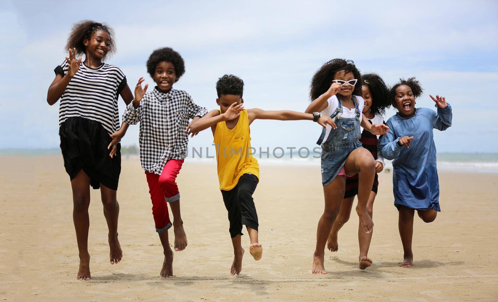 Kids playing running on sand at the beach, A group of children holding hands in a row on the beach in summer, rear view against sea and blue sky