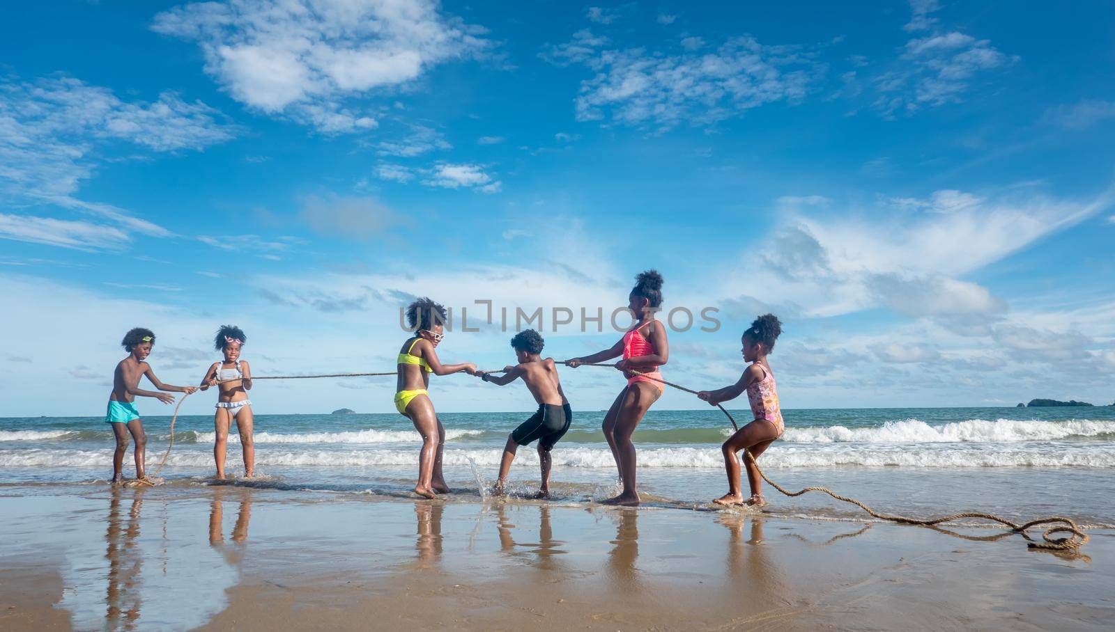 Kids playing running on sand at the beach, A group of children holding hands in a row on the beach in summer, rear view against sea and blue sky by chuanchai