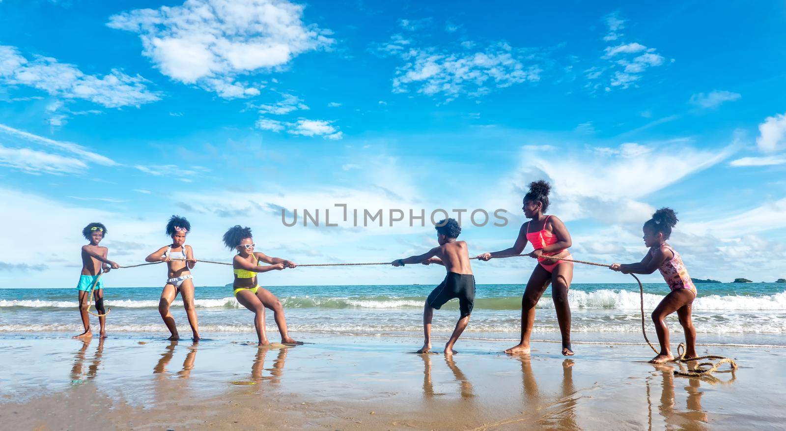 Kids playing running on sand at the beach, A group of children holding hands in a row on the beach in summer, rear view against sea and blue sky