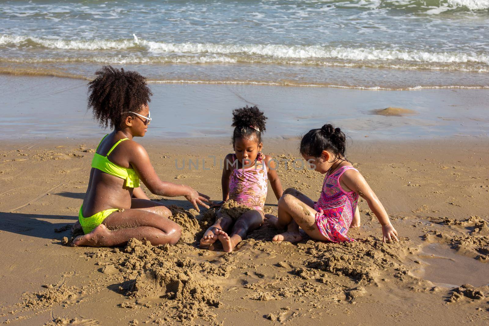 Kids playing running on sand at the beach, A group of children holding hands in a row on the beach in summer, rear view against sea and blue sky